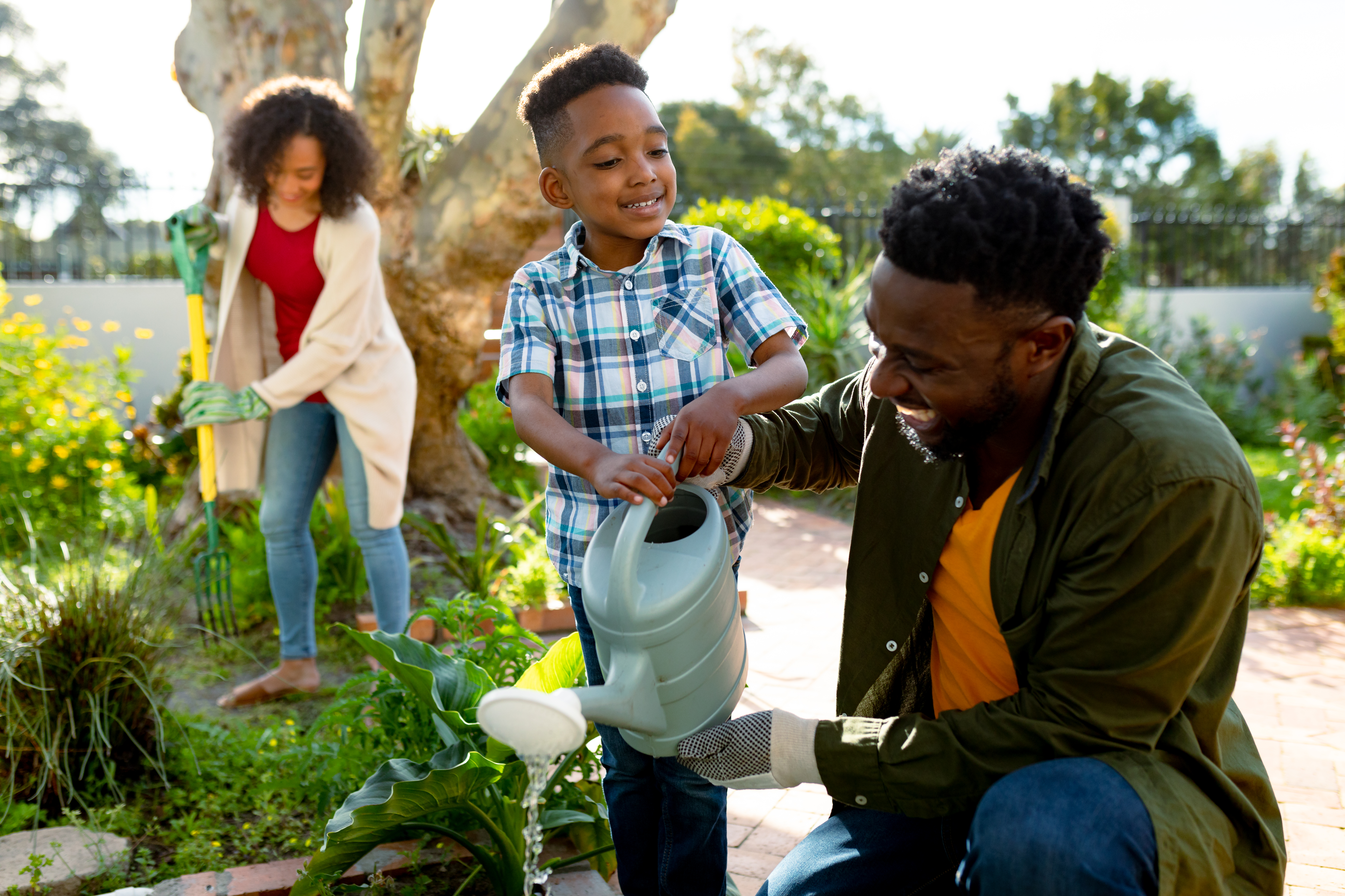 Happy african american father and son watering plants together. family time, having fun together at home and garden.